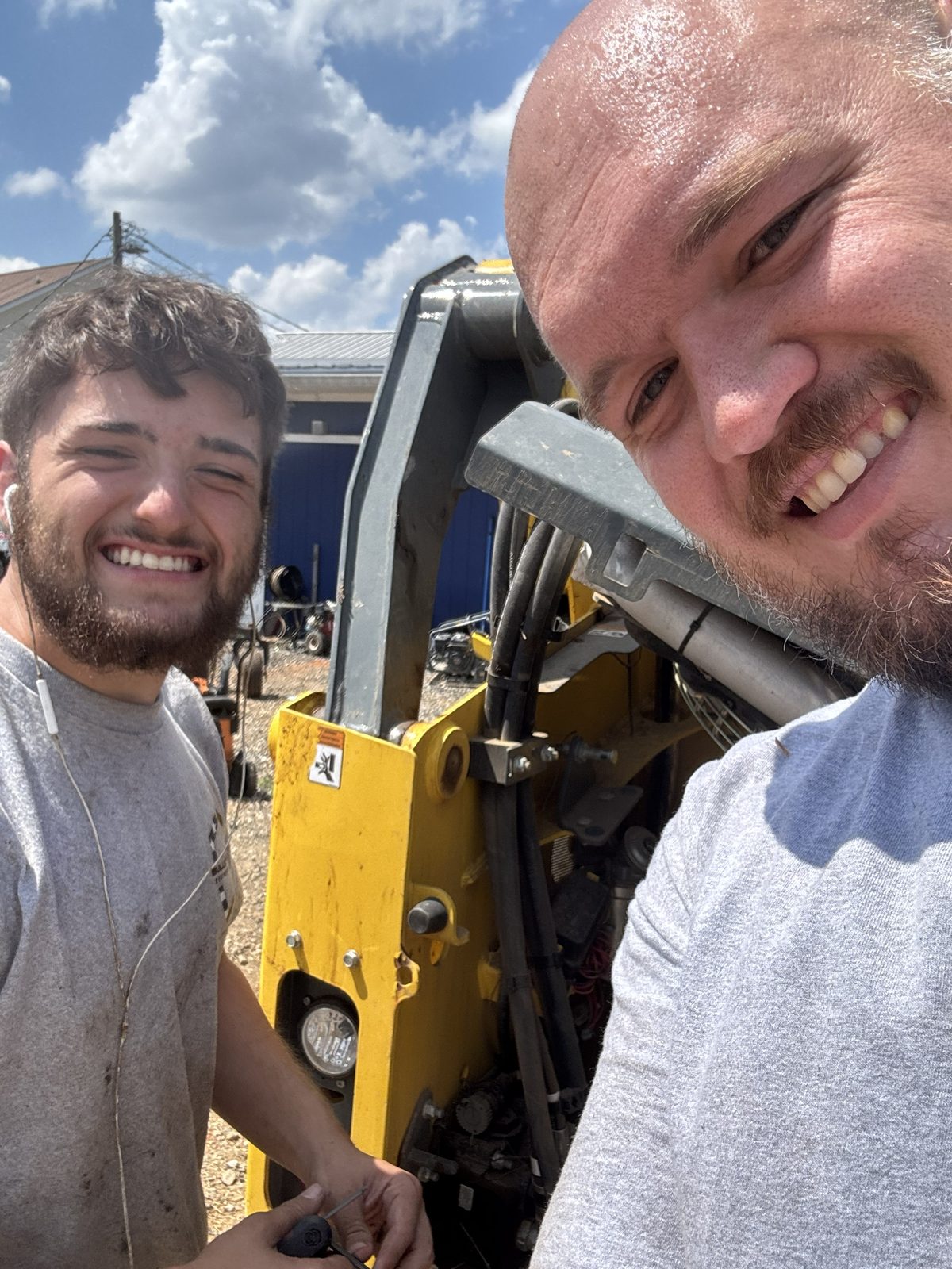 Rene and his son smiling while working on a skid steer at the Bulletproof yard